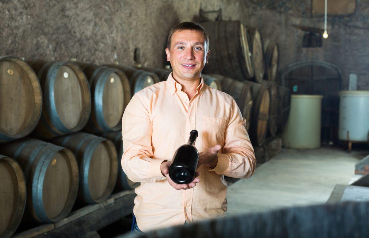 Handsome man posing with bottle of wine in winery cellar