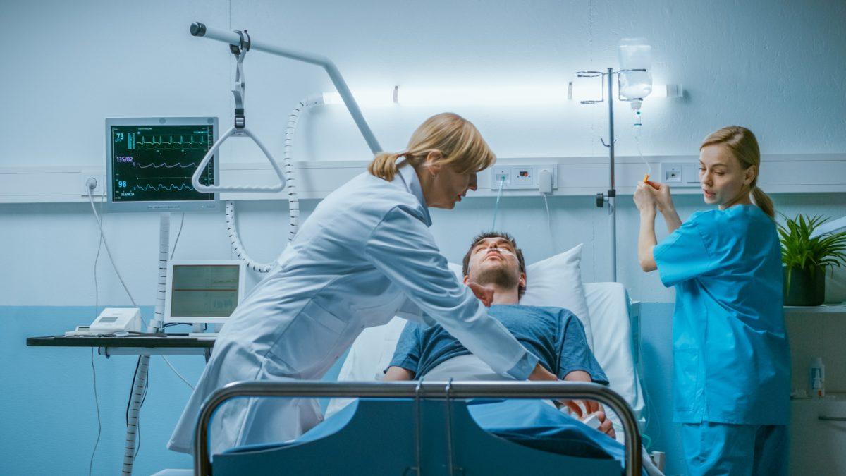Emergency in the Hospital Doctor and Nurse Rush into the Ward to Safe Dying Patient. Man is Lying on the Bed without Signs of Life. Doctors Do Everything to Resuscitate Him.