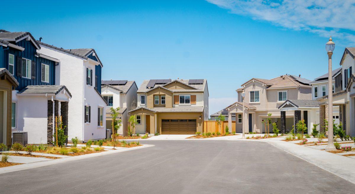 Taken from the middle of the street with homes on either side and blue sky in the background