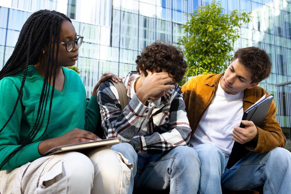 Friends consoling and comforting upset and depressed young male college student.Friendship concept.
